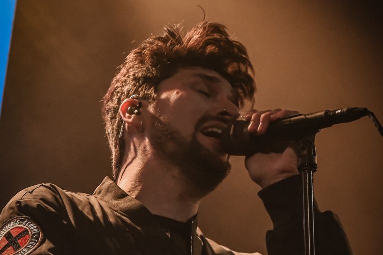 Welsh rock band Holding Absence vocalist Lucas Woodland singing passionately into a microphone during a live concert performance.